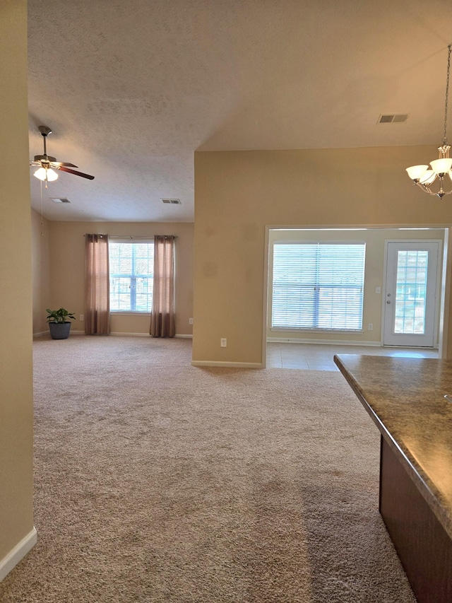 unfurnished living room featuring light carpet, a textured ceiling, visible vents, and baseboards