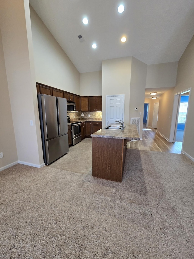 kitchen with a center island with sink, visible vents, light colored carpet, stainless steel appliances, and a sink