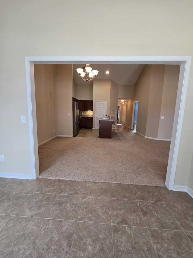 unfurnished living room featuring vaulted ceiling, a notable chandelier, dark carpet, and baseboards