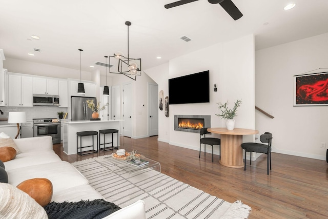 living room featuring ceiling fan with notable chandelier and dark hardwood / wood-style floors