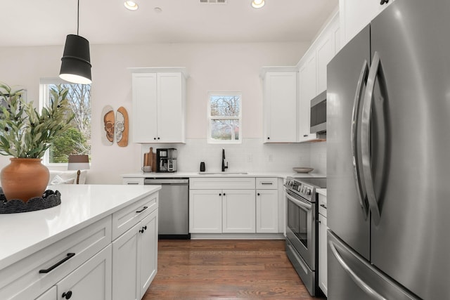 kitchen featuring white cabinetry, stainless steel appliances, sink, backsplash, and pendant lighting