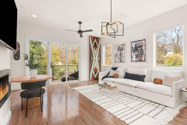 living room with ceiling fan with notable chandelier, light wood-type flooring, and a wealth of natural light