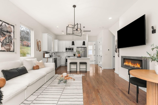 living room with sink, an inviting chandelier, and wood-type flooring