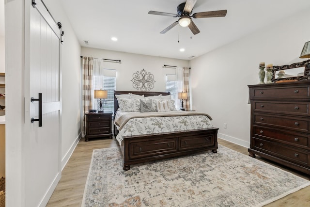 bedroom with a barn door, light wood-type flooring, recessed lighting, and baseboards