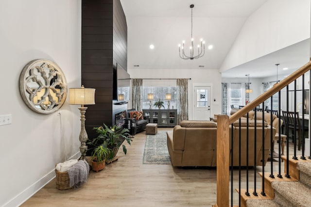 living room with a chandelier, stairs, light wood-type flooring, a fireplace, and high vaulted ceiling