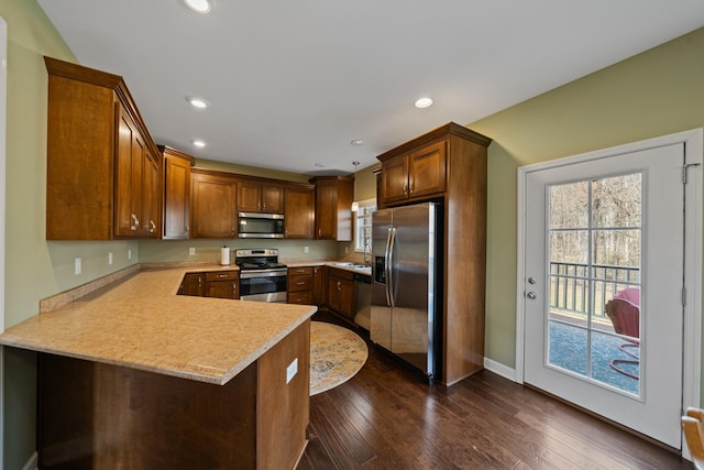 kitchen featuring kitchen peninsula, appliances with stainless steel finishes, a kitchen bar, and dark hardwood / wood-style floors