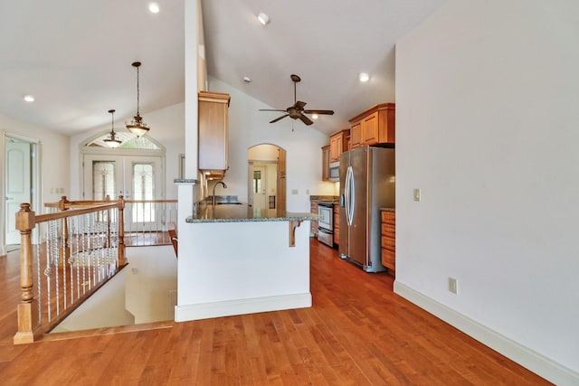 kitchen with appliances with stainless steel finishes, kitchen peninsula, hanging light fixtures, hardwood / wood-style flooring, and a breakfast bar area