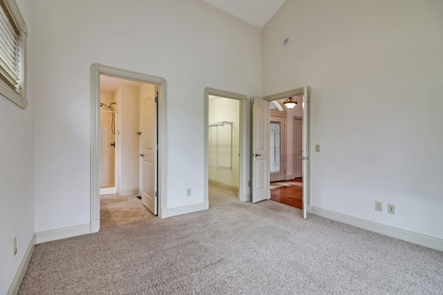 unfurnished bedroom with connected bathroom, high vaulted ceiling, a walk in closet, and light colored carpet