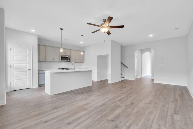 kitchen with a center island with sink, gray cabinetry, light hardwood / wood-style floors, ceiling fan, and pendant lighting