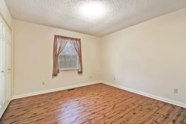 empty room featuring visible vents, a textured ceiling, baseboards, and wood finished floors