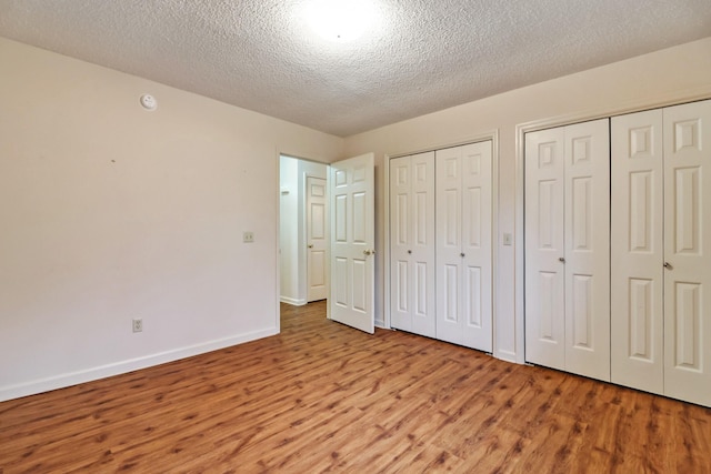 unfurnished bedroom with a textured ceiling, light wood-style flooring, baseboards, and two closets