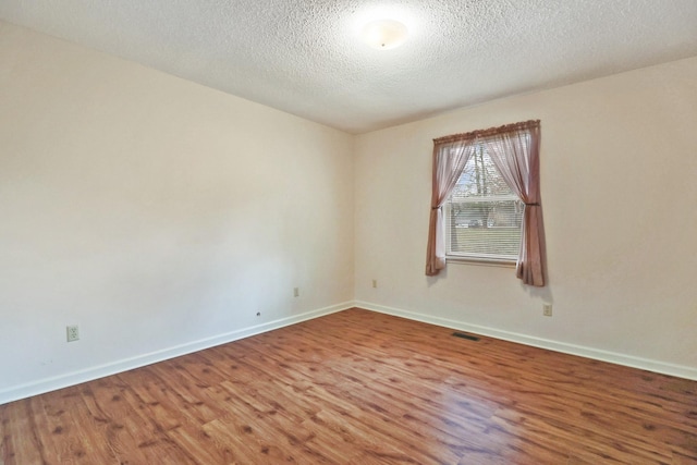 spare room with baseboards, a textured ceiling, visible vents, and wood finished floors