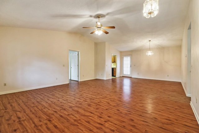 spare room with ceiling fan with notable chandelier, vaulted ceiling, dark wood finished floors, and baseboards