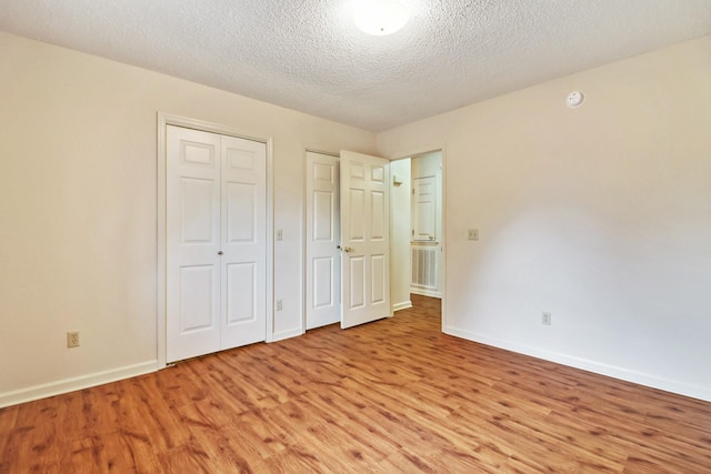 unfurnished bedroom with light wood-type flooring, a textured ceiling, baseboards, and two closets