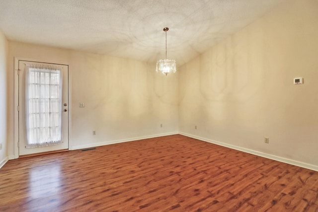 spare room featuring wood finished floors, a healthy amount of sunlight, visible vents, and an inviting chandelier