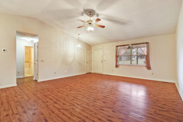 spare room with a textured ceiling, wood finished floors, a ceiling fan, baseboards, and vaulted ceiling