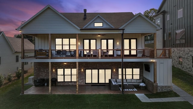 back house at dusk featuring outdoor lounge area, a patio, a lawn, and a balcony