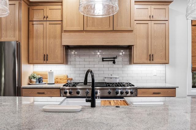 kitchen featuring ventilation hood, tasteful backsplash, light stone counters, and stainless steel fridge