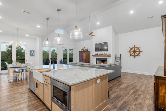 kitchen featuring a kitchen island with sink, light stone countertops, sink, appliances with stainless steel finishes, and pendant lighting