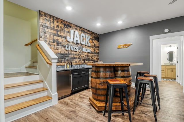 bar featuring sink, stainless steel dishwasher, and light hardwood / wood-style floors