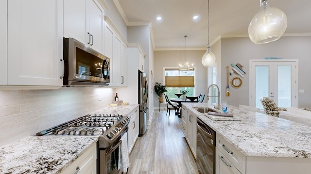 kitchen with a center island with sink, appliances with stainless steel finishes, white cabinetry, and decorative light fixtures