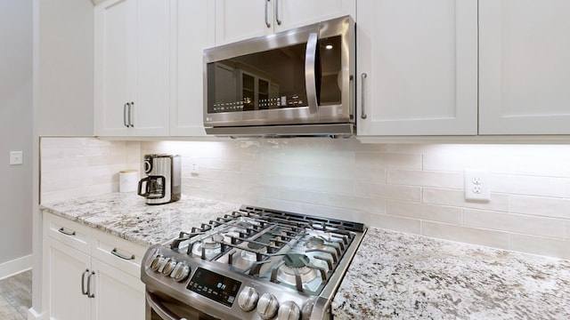 kitchen with appliances with stainless steel finishes, white cabinetry, light stone counters, and decorative backsplash