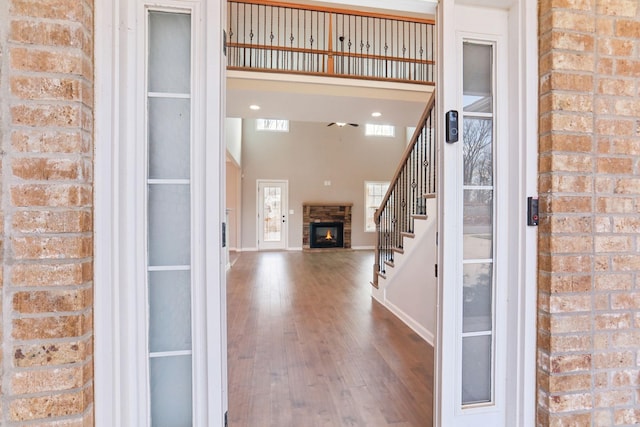 foyer with a brick fireplace, a towering ceiling, brick wall, and wood-type flooring