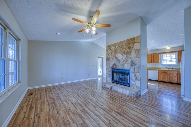 unfurnished living room featuring light hardwood / wood-style flooring, a stone fireplace, lofted ceiling, ceiling fan, and sink