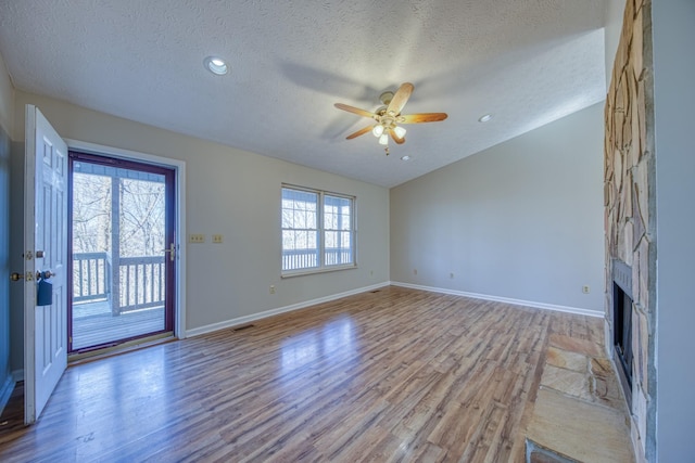 unfurnished living room featuring lofted ceiling, light hardwood / wood-style flooring, a textured ceiling, ceiling fan, and a fireplace