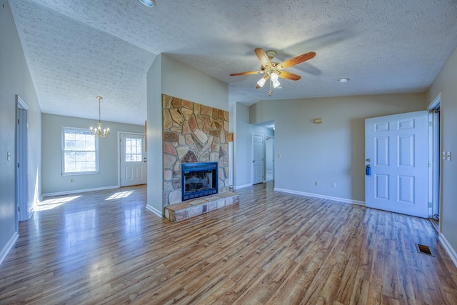 unfurnished living room with lofted ceiling, a stone fireplace, wood finished floors, baseboards, and ceiling fan with notable chandelier