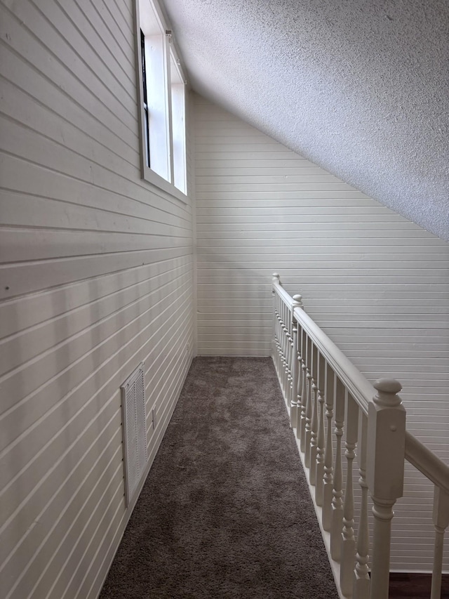 hallway featuring dark colored carpet, vaulted ceiling, and a textured ceiling