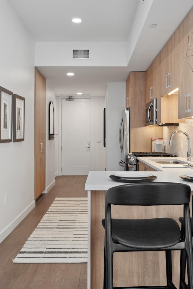 kitchen with a kitchen breakfast bar, appliances with stainless steel finishes, a peninsula, light countertops, and decorative backsplash