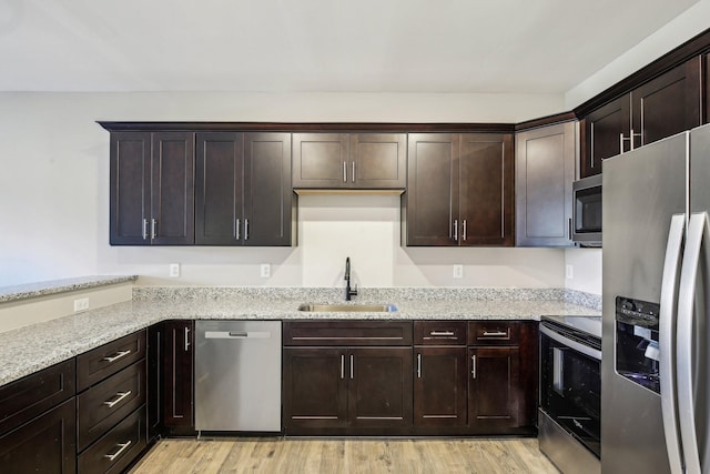 kitchen featuring appliances with stainless steel finishes, light wood-style floors, a sink, and light stone countertops