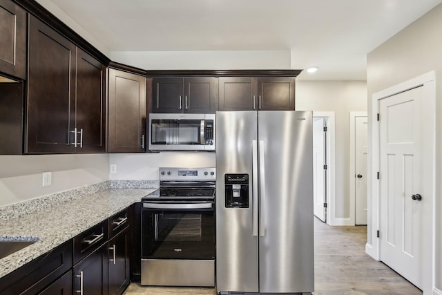 kitchen featuring light stone counters, stainless steel appliances, baseboards, dark brown cabinets, and light wood finished floors