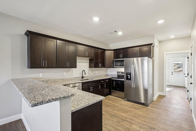 kitchen featuring dark brown cabinetry, visible vents, appliances with stainless steel finishes, light stone counters, and a sink