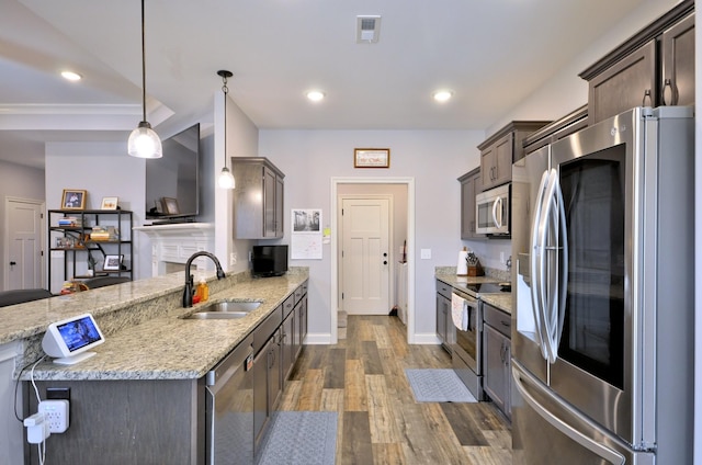 kitchen featuring appliances with stainless steel finishes, dark brown cabinets, light stone counters, decorative light fixtures, and sink