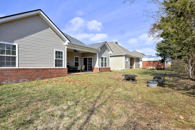 back of property with ceiling fan, a lawn, a patio area, and a fire pit