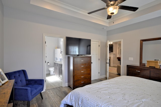 bedroom featuring a tray ceiling, light hardwood / wood-style floors, and ensuite bath