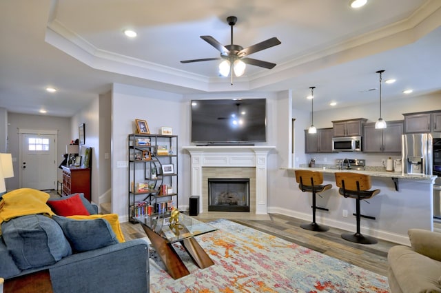 living room featuring a tile fireplace, ceiling fan, a tray ceiling, ornamental molding, and dark hardwood / wood-style flooring