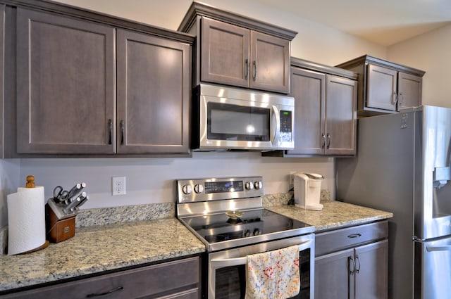 kitchen with appliances with stainless steel finishes, light stone countertops, and dark brown cabinets
