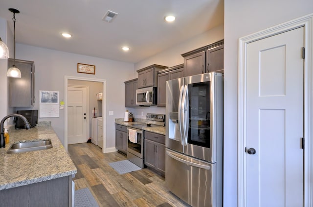 kitchen featuring stainless steel appliances, decorative light fixtures, sink, independent washer and dryer, and light stone counters