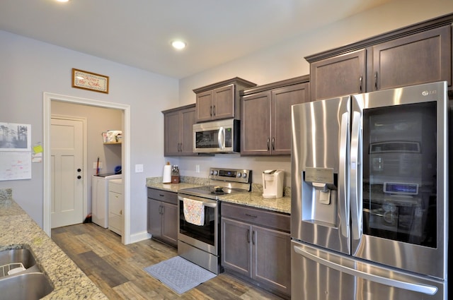 kitchen with dark brown cabinets, light stone counters, wood-type flooring, appliances with stainless steel finishes, and separate washer and dryer