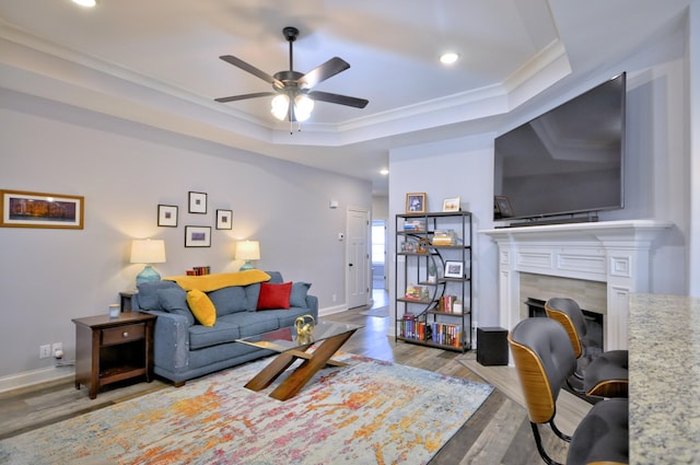 living room featuring light hardwood / wood-style flooring, ceiling fan, crown molding, a raised ceiling, and a fireplace