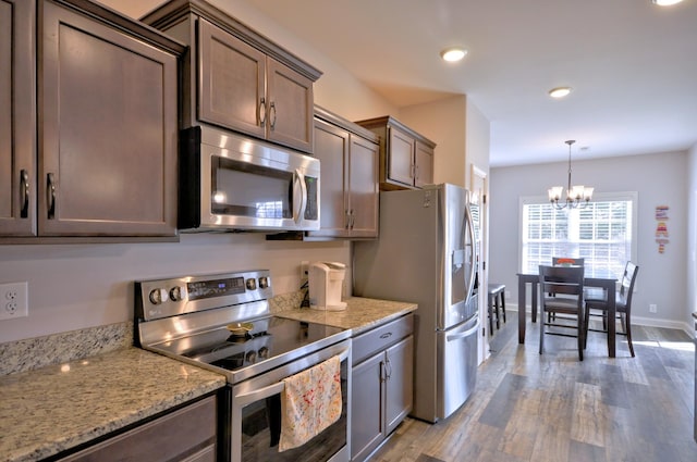 kitchen with dark brown cabinetry, hanging light fixtures, stainless steel appliances, and light stone counters