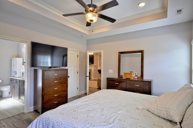 bedroom featuring a raised ceiling, ensuite bathroom, and hardwood / wood-style flooring