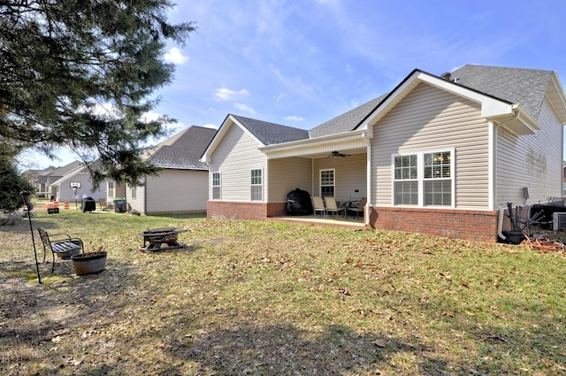 back of property featuring ceiling fan, a lawn, a patio, and a fire pit