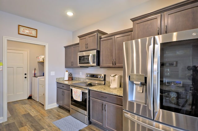 kitchen featuring independent washer and dryer, light stone countertops, stainless steel appliances, hardwood / wood-style flooring, and dark brown cabinetry