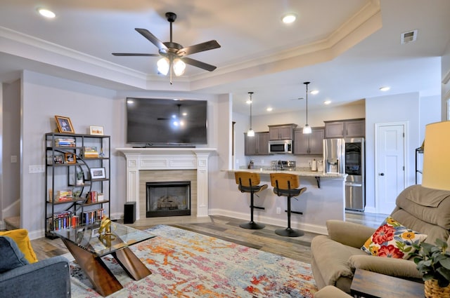living room with a tray ceiling, a tile fireplace, crown molding, and light hardwood / wood-style flooring