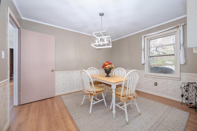 dining room with crown molding, wainscoting, wood finished floors, baseboards, and an inviting chandelier
