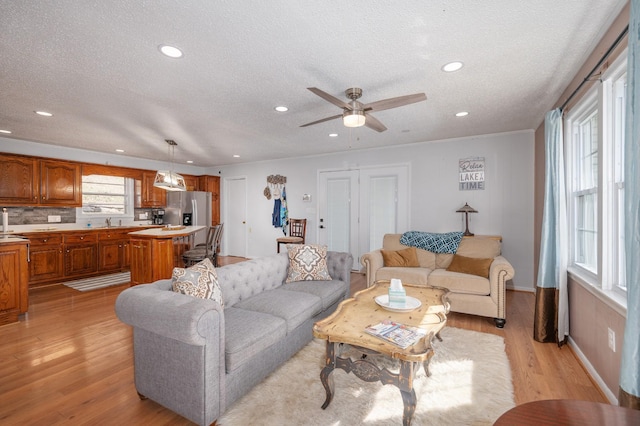 living room with recessed lighting, a textured ceiling, a ceiling fan, and light wood-style flooring